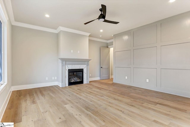 unfurnished living room with ceiling fan, ornamental molding, a high end fireplace, and light hardwood / wood-style flooring