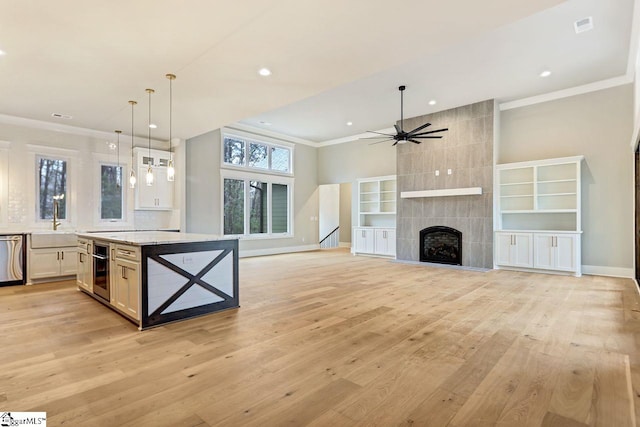 kitchen featuring a tile fireplace, light hardwood / wood-style floors, ornamental molding, ceiling fan, and light stone counters