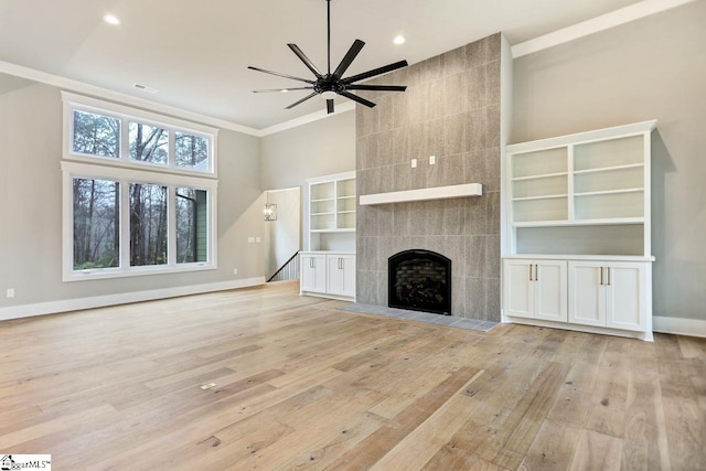 unfurnished living room featuring a fireplace, a high ceiling, ornamental molding, light hardwood / wood-style flooring, and ceiling fan