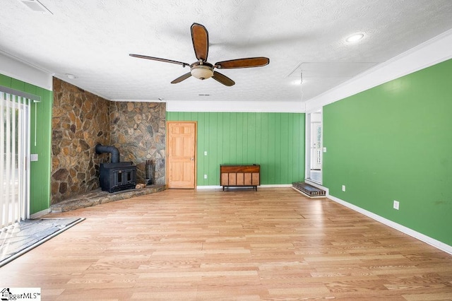 unfurnished living room with a wood stove, plenty of natural light, and ceiling fan