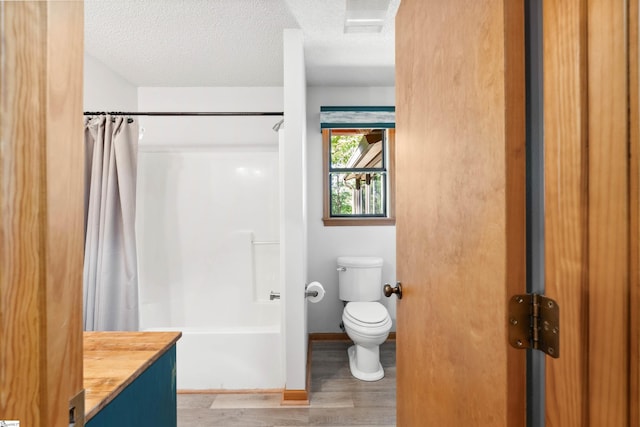 full bathroom featuring hardwood / wood-style floors, toilet, shower / tub combo, vanity, and a textured ceiling