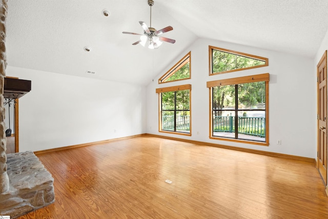 living room featuring light wood-type flooring, a textured ceiling, ceiling fan, and a stone fireplace