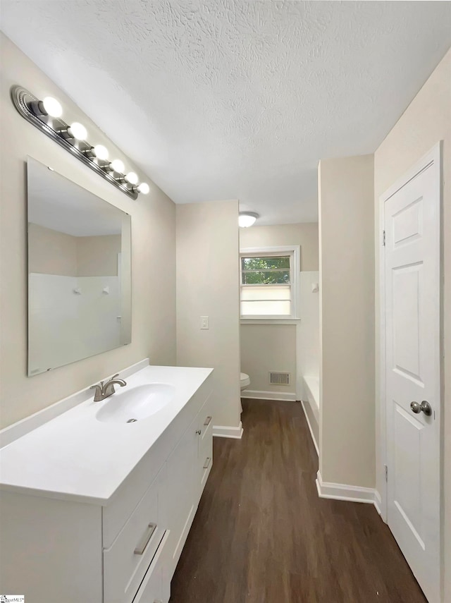 bathroom featuring toilet, walk in shower, vanity, a textured ceiling, and wood-type flooring