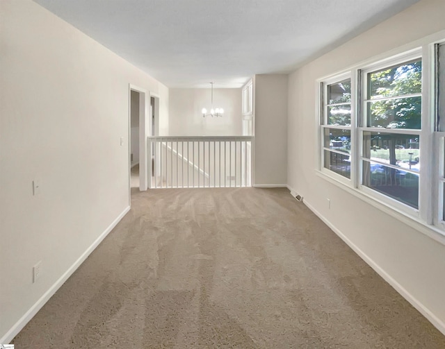 carpeted empty room featuring an inviting chandelier