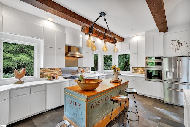 kitchen featuring a wealth of natural light, beamed ceiling, wall chimney exhaust hood, and white cabinets