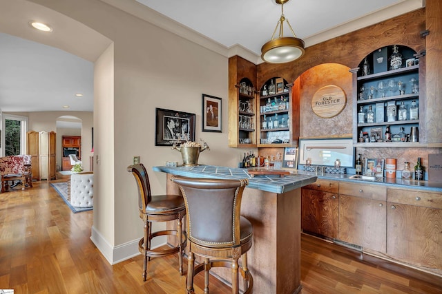 bar with decorative light fixtures, hardwood / wood-style floors, and tile counters