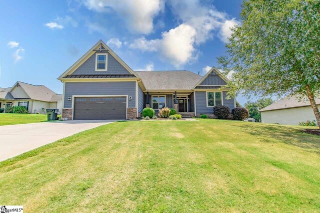 craftsman-style home featuring a standing seam roof, stone siding, a front lawn, and concrete driveway