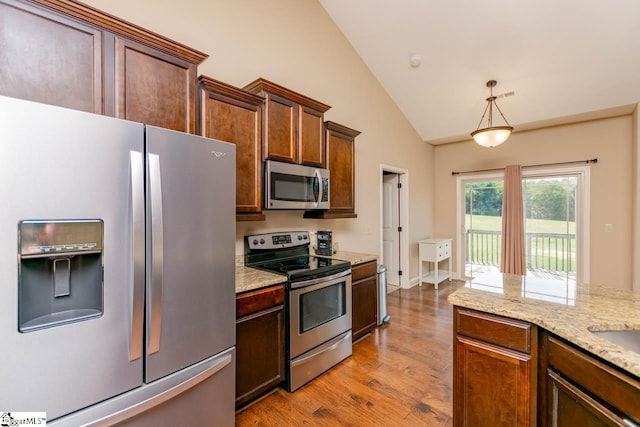 kitchen with hanging light fixtures, light stone counters, stainless steel appliances, light hardwood / wood-style floors, and lofted ceiling