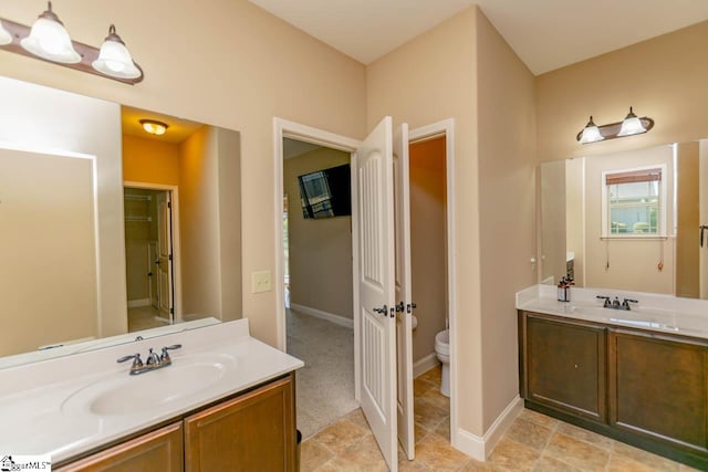 full bath featuring two vanities, a sink, toilet, and baseboards