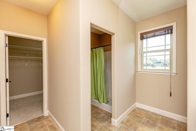 full bath featuring curtained shower, stone finish floor, a spacious closet, and baseboards