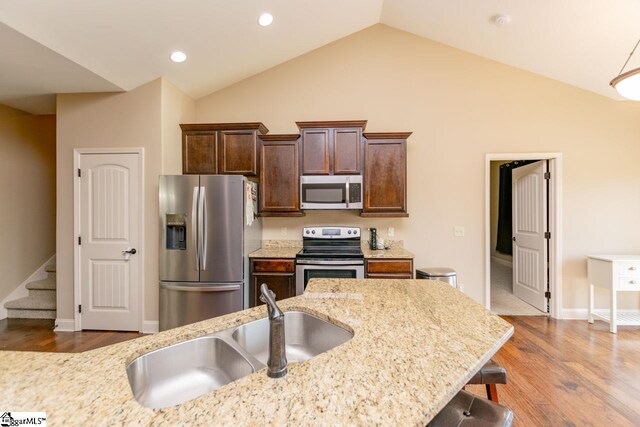 kitchen with appliances with stainless steel finishes, light stone countertops, sink, dark wood-type flooring, and a breakfast bar