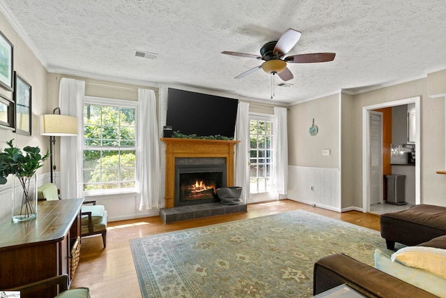 living room featuring a wealth of natural light, light hardwood / wood-style flooring, ornamental molding, and a tiled fireplace