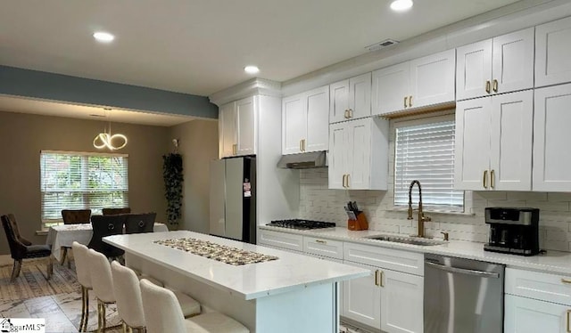 kitchen with light wood-type flooring, stainless steel appliances, white cabinets, sink, and decorative light fixtures