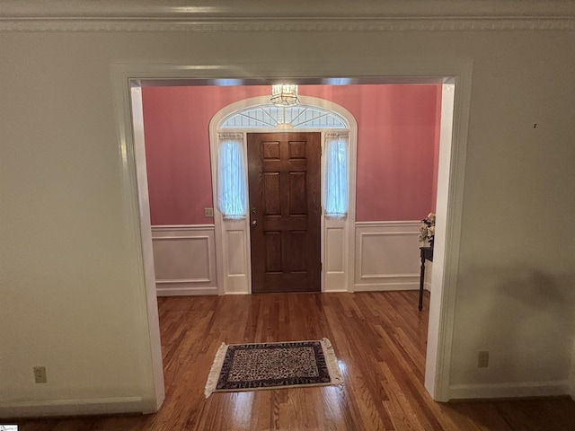 foyer featuring a wainscoted wall, ornamental molding, wood finished floors, and a decorative wall