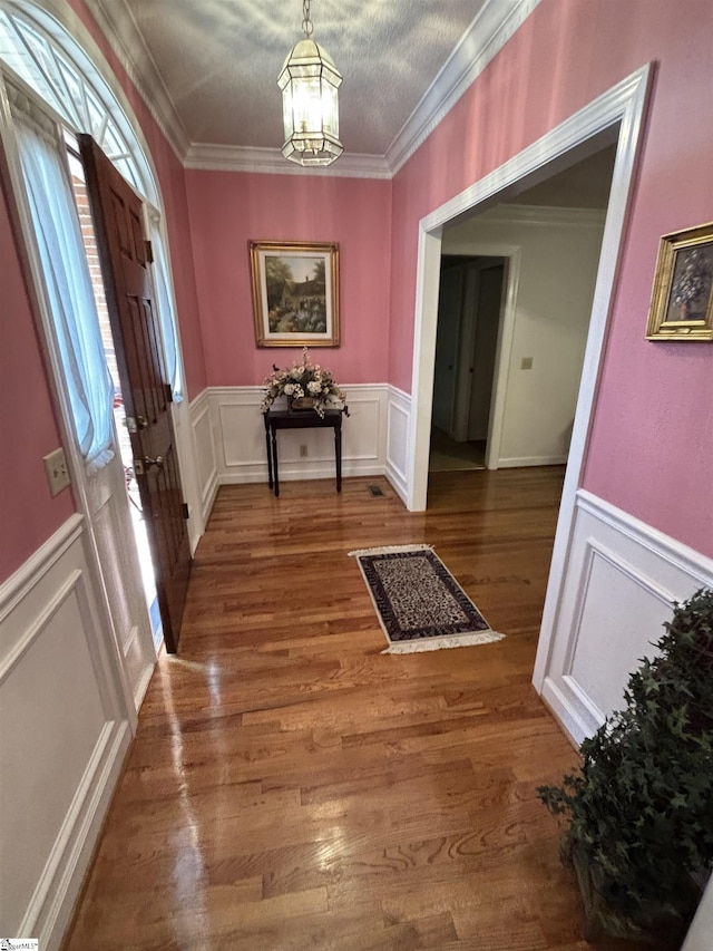 foyer featuring a notable chandelier, a decorative wall, wood finished floors, wainscoting, and crown molding