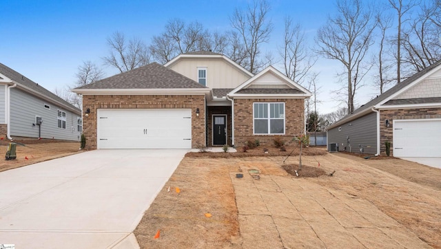 craftsman-style house featuring brick siding, roof with shingles, central air condition unit, an attached garage, and driveway