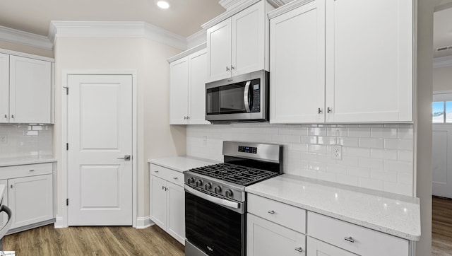 kitchen with crown molding, light wood-type flooring, stainless steel appliances, light stone countertops, and white cabinets