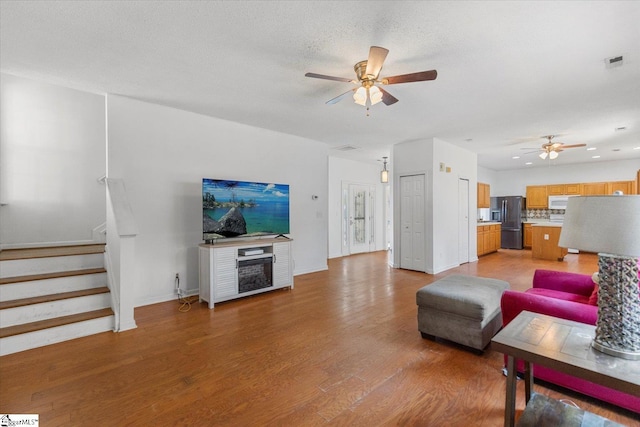 living room with ceiling fan, light hardwood / wood-style floors, and a textured ceiling