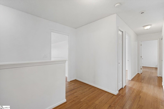 hallway with a textured ceiling and light hardwood / wood-style floors