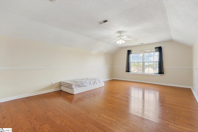 additional living space with a textured ceiling, ceiling fan, wood-type flooring, and lofted ceiling