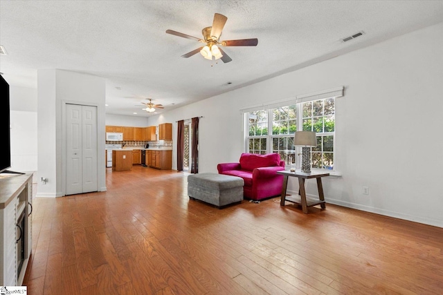 living room with a textured ceiling, light hardwood / wood-style floors, and ceiling fan