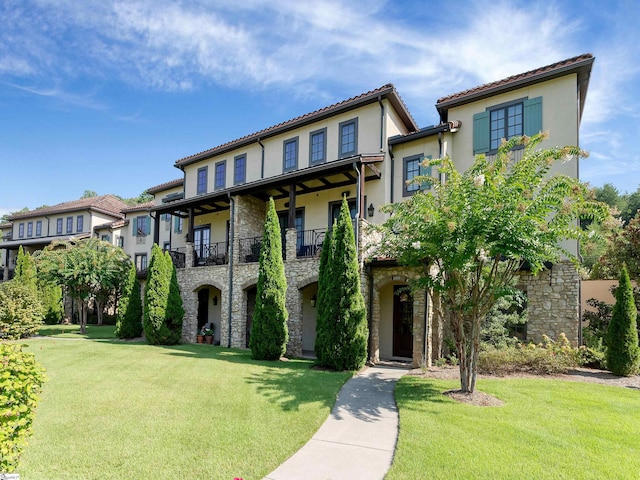 mediterranean / spanish house with a balcony, stone siding, stucco siding, and a front lawn