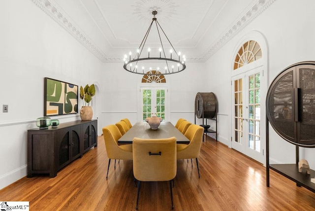 dining space featuring wood-type flooring, crown molding, a notable chandelier, and french doors