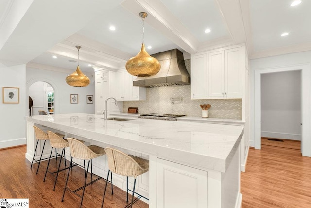 kitchen with decorative light fixtures, custom exhaust hood, white cabinetry, and light hardwood / wood-style flooring