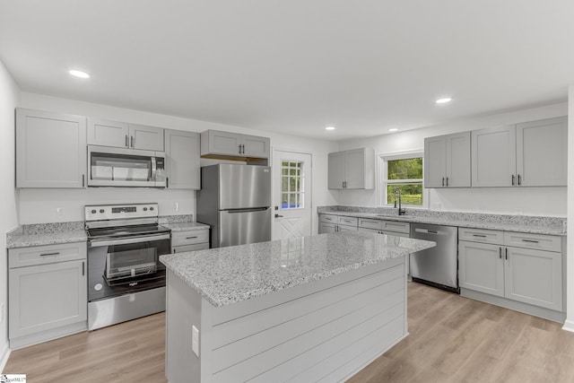 kitchen with a center island, light wood-type flooring, appliances with stainless steel finishes, light stone countertops, and sink