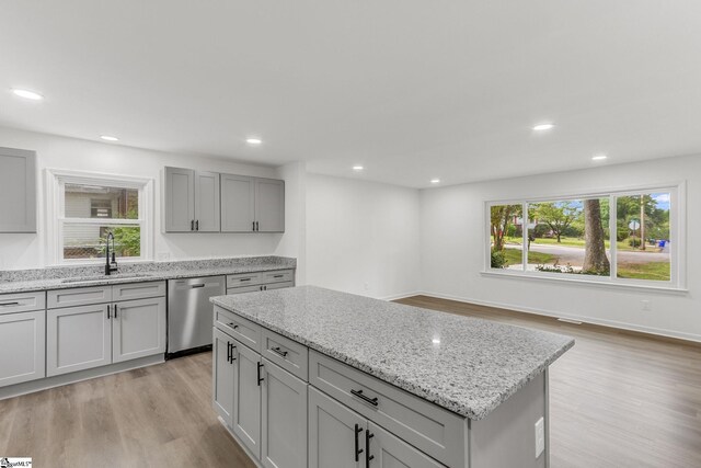 kitchen with light wood-type flooring, light stone counters, sink, a kitchen island, and stainless steel dishwasher