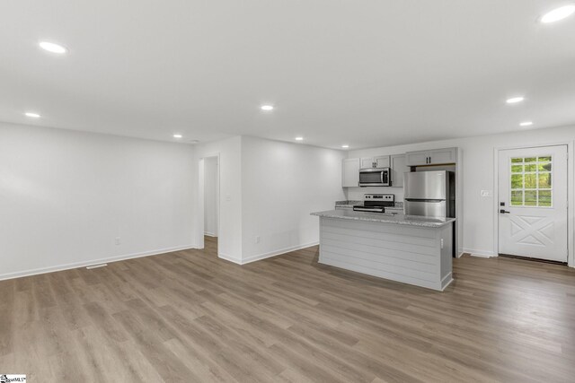 kitchen with a kitchen island, stainless steel appliances, light stone countertops, and light wood-type flooring