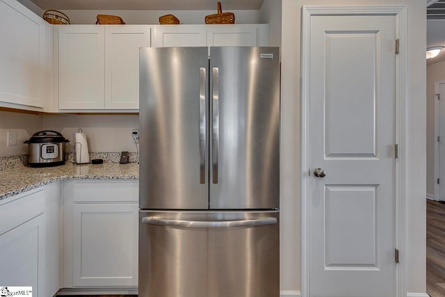 kitchen featuring light stone countertops, stainless steel fridge, hardwood / wood-style flooring, and white cabinets