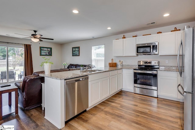 kitchen with white cabinets, appliances with stainless steel finishes, hardwood / wood-style floors, and kitchen peninsula