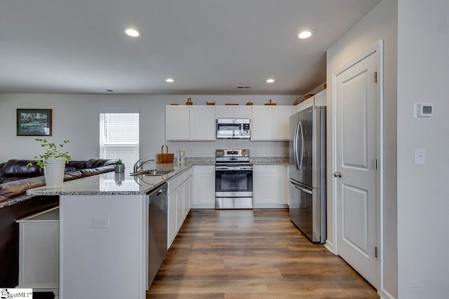 kitchen featuring appliances with stainless steel finishes, kitchen peninsula, sink, hardwood / wood-style flooring, and light stone counters