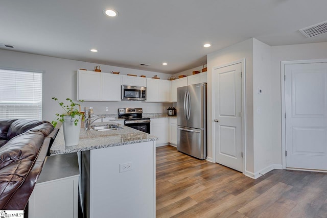 kitchen with stainless steel appliances, light stone countertops, kitchen peninsula, and light hardwood / wood-style floors