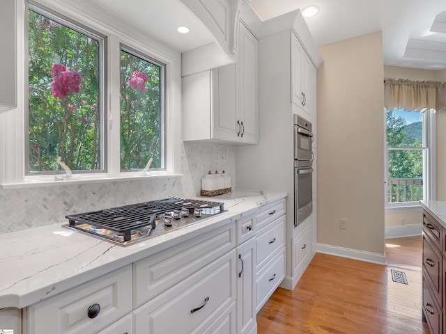 kitchen with white cabinets, backsplash, stainless steel appliances, and light hardwood / wood-style flooring