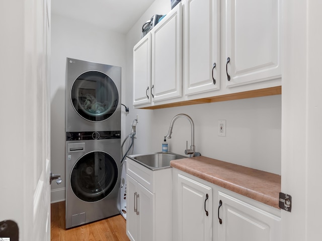 clothes washing area featuring stacked washing maching and dryer, cabinets, sink, and light wood-type flooring