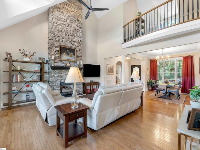 living room with light wood-type flooring, ceiling fan with notable chandelier, high vaulted ceiling, and a fireplace