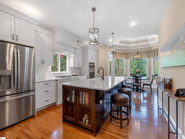 kitchen with light hardwood / wood-style flooring, pendant lighting, appliances with stainless steel finishes, an island with sink, and light stone counters