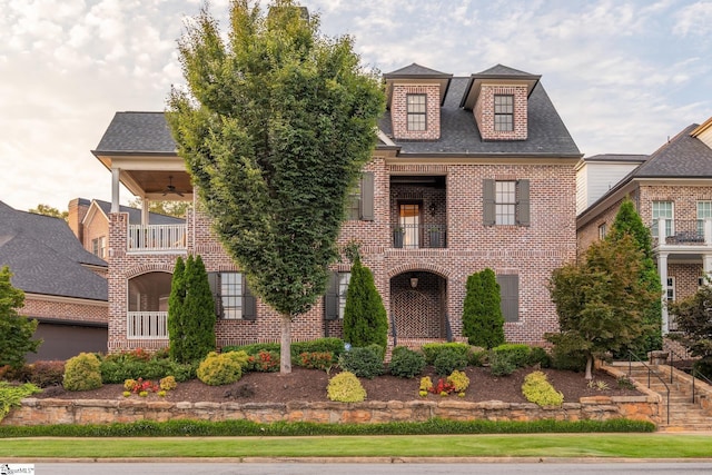 view of front of home with a balcony, roof with shingles, and brick siding