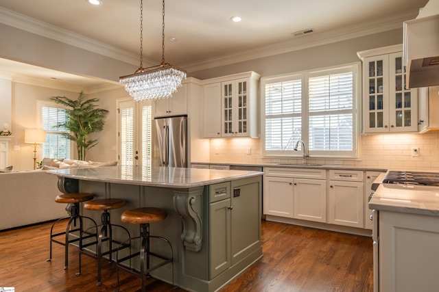 kitchen with ornamental molding, decorative light fixtures, stainless steel appliances, a center island, and light stone countertops