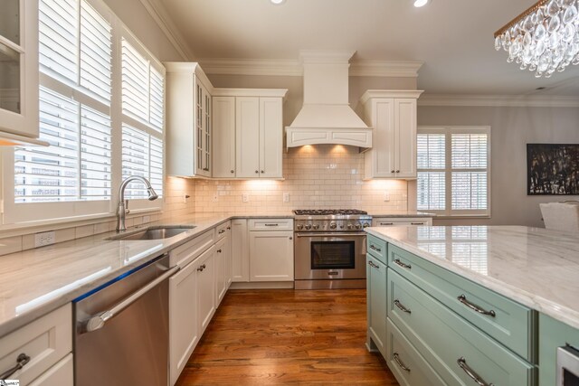 kitchen with white cabinets, custom exhaust hood, stainless steel appliances, crown molding, and a sink