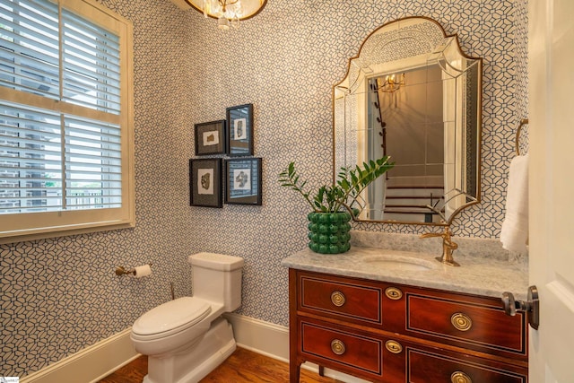 bathroom with toilet, wallpapered walls, baseboards, and vanity