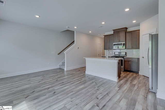 kitchen with light wood-type flooring, appliances with stainless steel finishes, tasteful backsplash, and a center island with sink