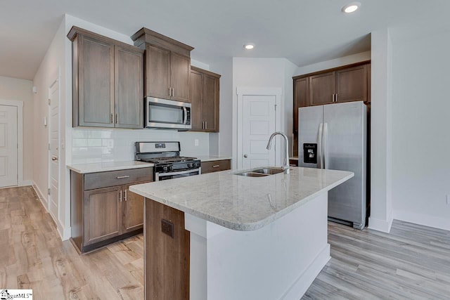 kitchen featuring an island with sink, stainless steel appliances, sink, and light stone counters