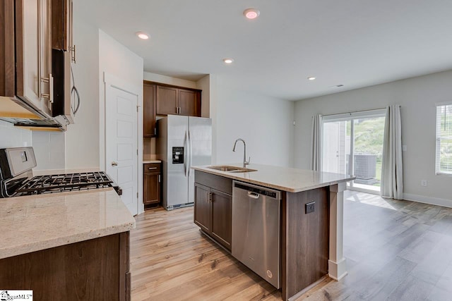 kitchen with a kitchen island with sink, light hardwood / wood-style flooring, stainless steel appliances, sink, and light stone countertops