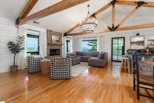 living room with light hardwood / wood-style flooring, wood walls, vaulted ceiling with beams, and a stone fireplace