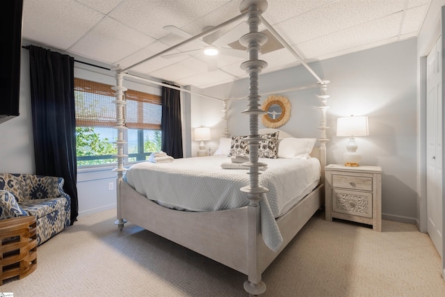 bedroom with a paneled ceiling, light colored carpet, and ceiling fan