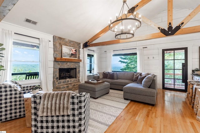 living room with a stone fireplace, light wood-type flooring, and vaulted ceiling with beams