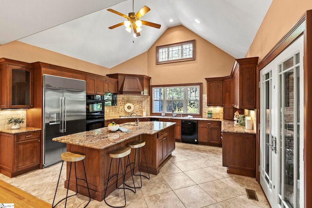 kitchen featuring black appliances, ceiling fan, an island with sink, and tasteful backsplash